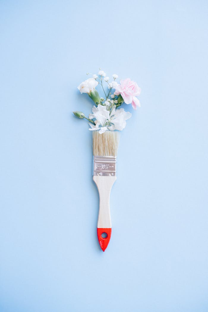 A minimalist image of a paintbrush adorned with delicate flowers against a blue background.